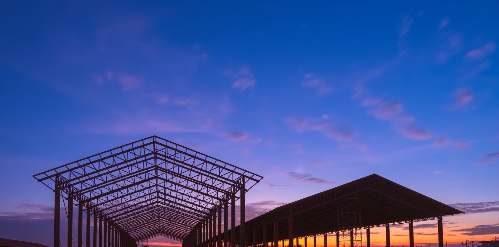 Silhouette two metal industrial buildings structure against sunset sky background in panoramic view